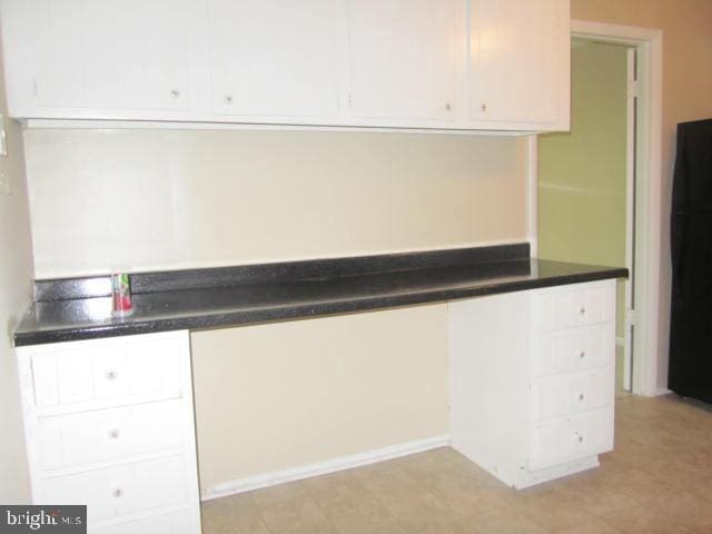 kitchen featuring built in desk, white cabinets, and black fridge