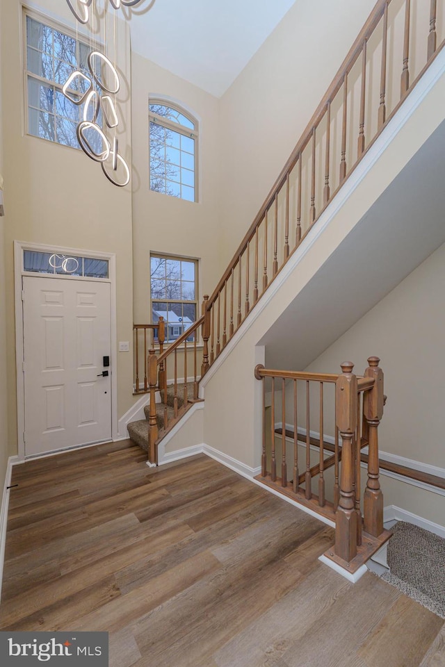 entrance foyer featuring a notable chandelier, wood finished floors, a high ceiling, baseboards, and stairs