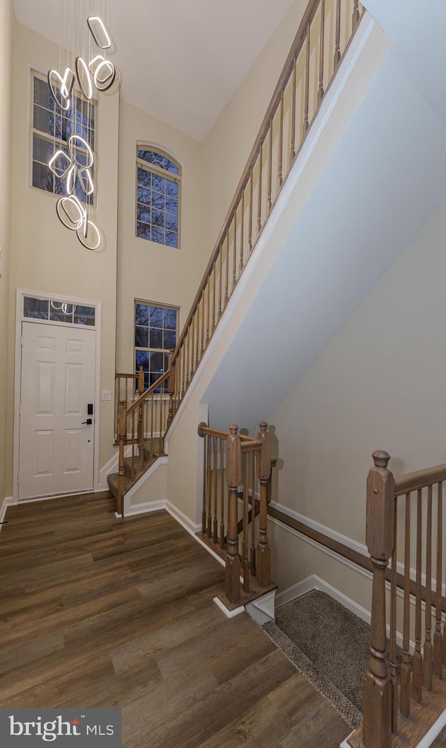 entryway with wood finished floors, baseboards, a high ceiling, stairs, and a notable chandelier