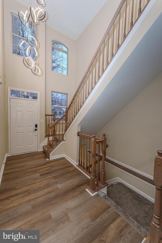 entrance foyer with baseboards, stairs, a high ceiling, wood finished floors, and a notable chandelier