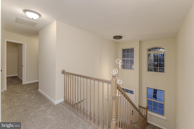 hall with carpet, visible vents, an upstairs landing, and baseboards