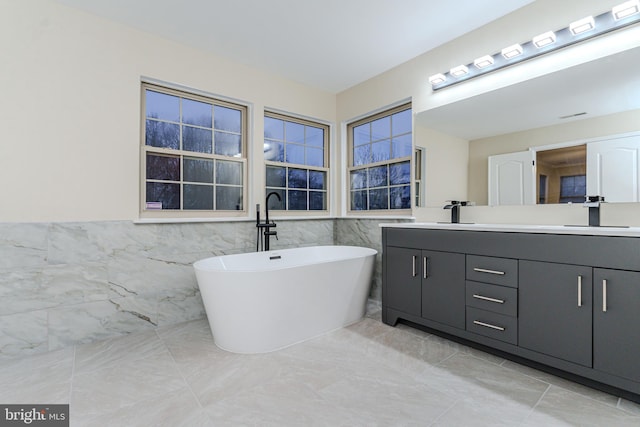 bathroom with double vanity, a soaking tub, tile walls, and a sink