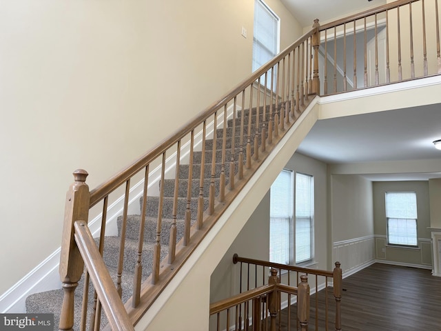 stairs with wood finished floors, a wainscoted wall, a towering ceiling, and baseboards