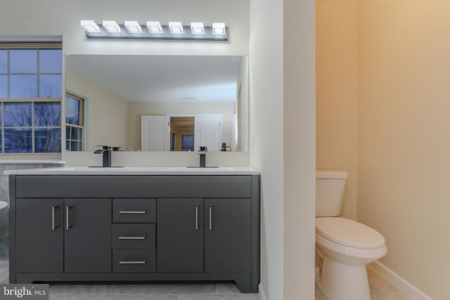 bathroom with toilet, a sink, tile patterned flooring, double vanity, and baseboards