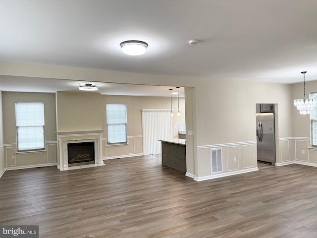 unfurnished living room featuring a premium fireplace, wood-type flooring, and an inviting chandelier