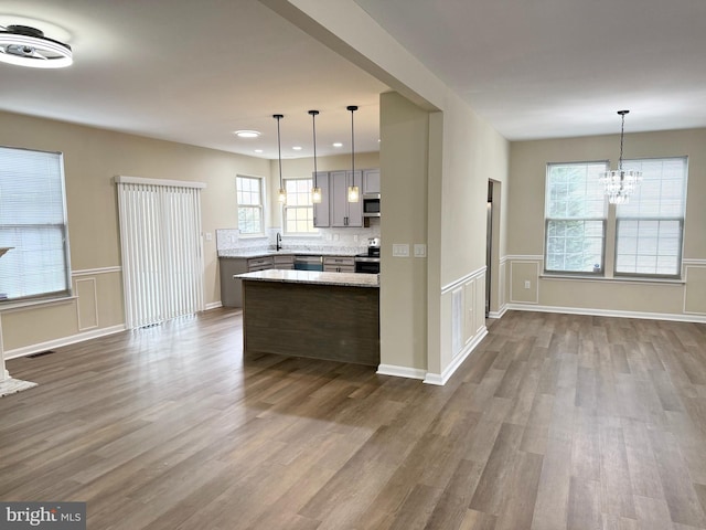 kitchen featuring appliances with stainless steel finishes, gray cabinetry, hardwood / wood-style floors, light stone countertops, and decorative light fixtures