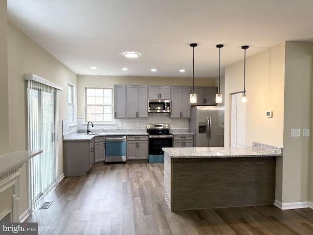 kitchen featuring appliances with stainless steel finishes, sink, hanging light fixtures, light stone counters, and kitchen peninsula