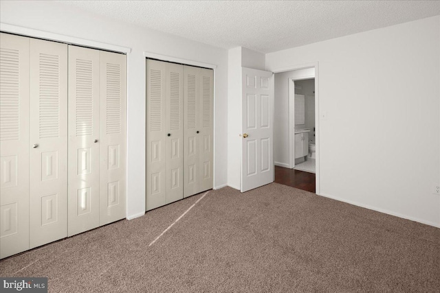 unfurnished bedroom with multiple closets, dark carpet, and a textured ceiling