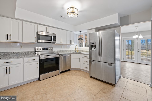 kitchen with sink, appliances with stainless steel finishes, white cabinetry, light stone counters, and a notable chandelier