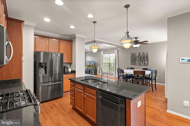 kitchen with sink, hanging light fixtures, light wood-type flooring, appliances with stainless steel finishes, and an island with sink