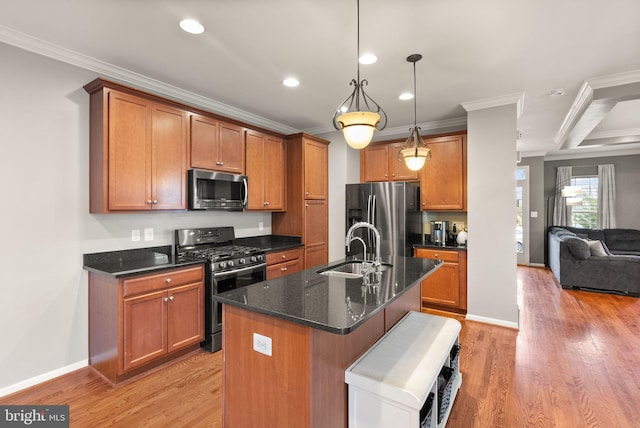 kitchen with sink, hanging light fixtures, stainless steel appliances, ornamental molding, and an island with sink