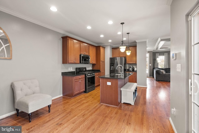 kitchen with hanging light fixtures, appliances with stainless steel finishes, a kitchen island with sink, and light hardwood / wood-style flooring