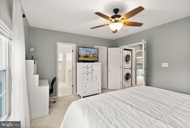 carpeted bedroom featuring ceiling fan, ensuite bath, stacked washer / dryer, and multiple windows