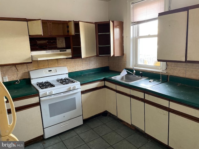 kitchen with white range with gas cooktop, sink, backsplash, and dark tile patterned flooring