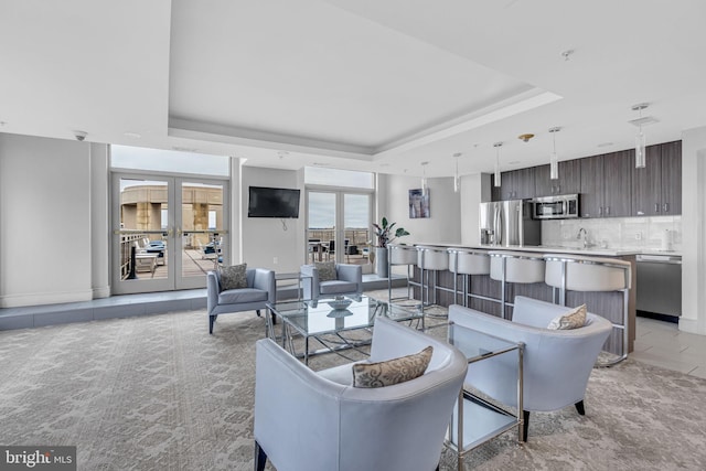 living room with a raised ceiling, sink, light colored carpet, and french doors