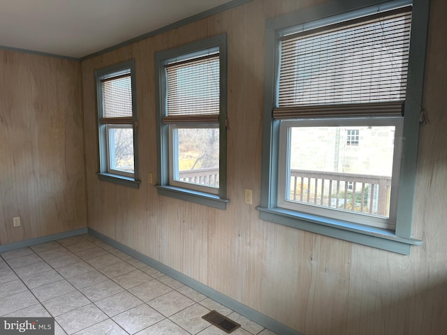 tiled spare room with ornamental molding and wood walls