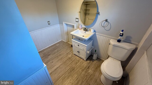 bathroom with toilet, vanity, wood finished floors, and wainscoting