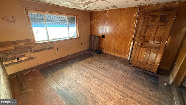 empty room featuring wooden walls, radiator heating unit, and wood finished floors