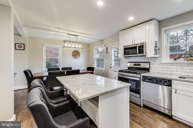 kitchen featuring white cabinetry, hanging light fixtures, a kitchen island, stainless steel appliances, and light stone countertops