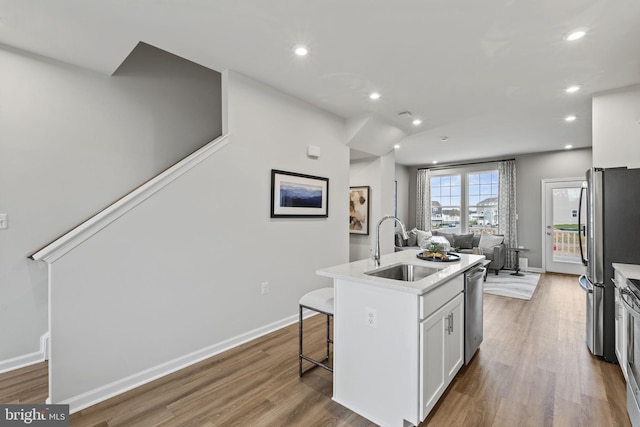 kitchen with sink, hardwood / wood-style flooring, appliances with stainless steel finishes, an island with sink, and white cabinets