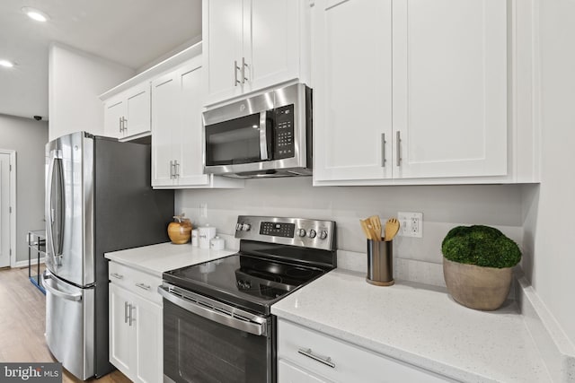 kitchen with white cabinetry, stainless steel appliances, light stone counters, and light hardwood / wood-style flooring