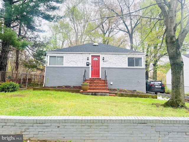 view of front of property featuring a front yard, fence, brick siding, and roof with shingles