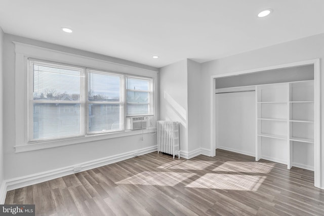 unfurnished bedroom with wood-type flooring, radiator, cooling unit, and a closet