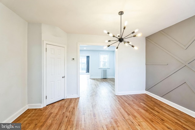 unfurnished room with an inviting chandelier, radiator, and light wood-type flooring