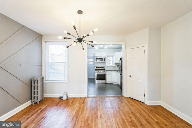 unfurnished living room with a notable chandelier, radiator heating unit, and light wood-type flooring