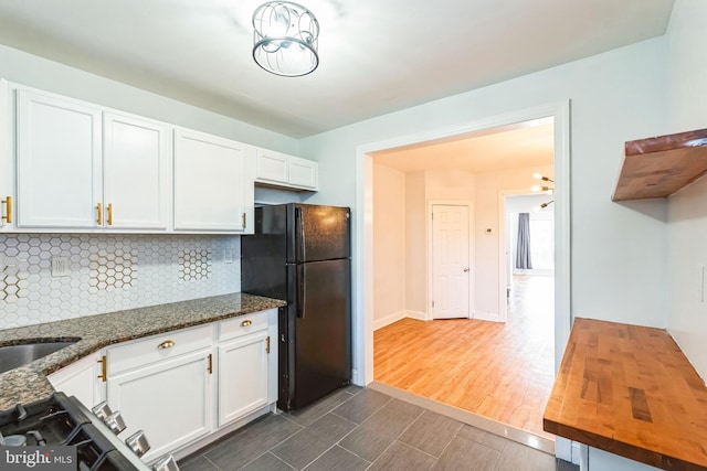 kitchen featuring decorative backsplash, black refrigerator, white cabinets, and dark stone counters