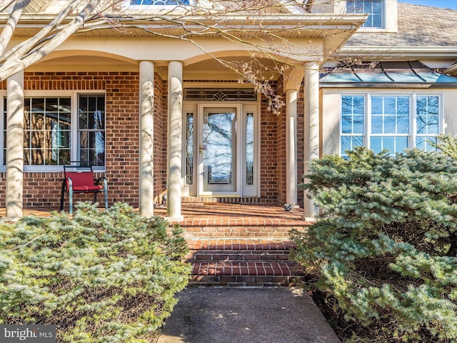 entrance to property featuring a shingled roof and brick siding