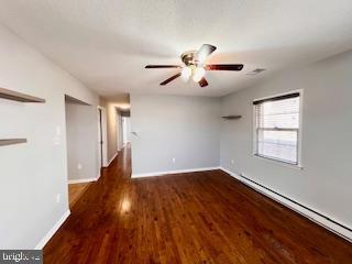 unfurnished room featuring ceiling fan, dark hardwood / wood-style floors, and a baseboard heating unit