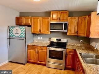 kitchen with sink, light hardwood / wood-style flooring, stainless steel appliances, and light stone countertops