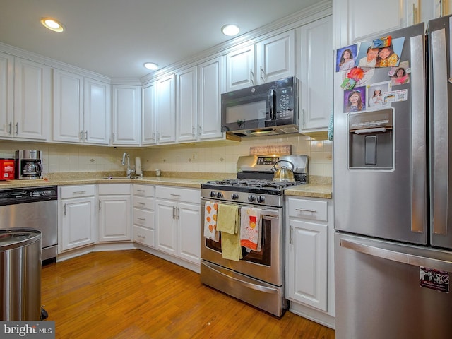 kitchen with sink, white cabinetry, light wood-type flooring, appliances with stainless steel finishes, and decorative backsplash