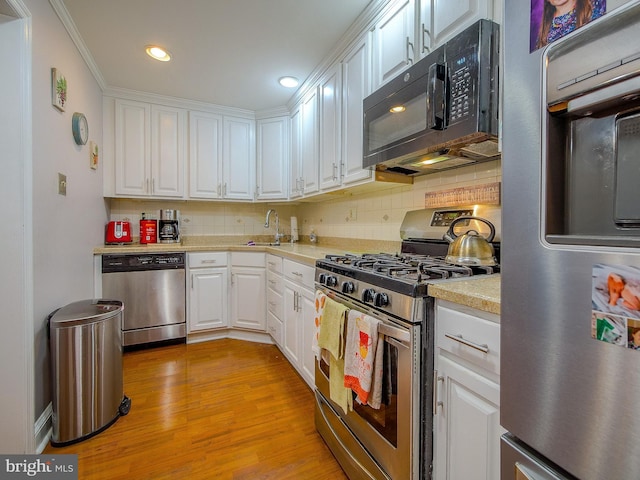 kitchen featuring appliances with stainless steel finishes, white cabinetry, sink, decorative backsplash, and light hardwood / wood-style flooring