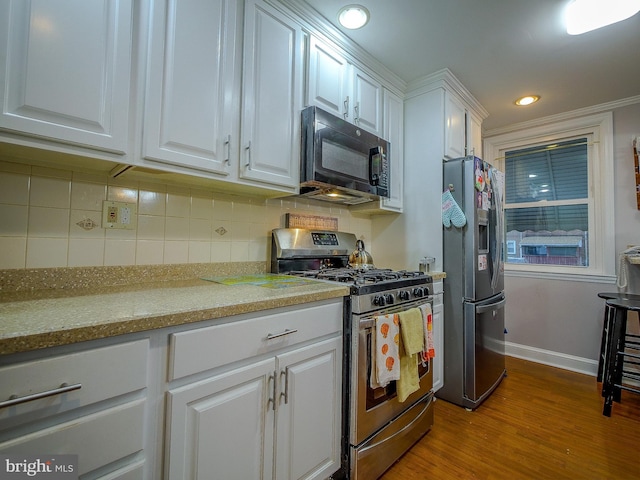 kitchen with light hardwood / wood-style flooring, appliances with stainless steel finishes, white cabinetry, backsplash, and light stone counters