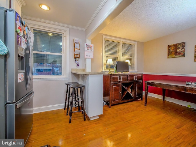 bar with stainless steel fridge with ice dispenser, crown molding, light hardwood / wood-style floors, and a textured ceiling