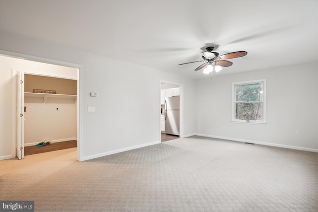 unfurnished bedroom with stainless steel fridge, ceiling fan, carpet, connected bathroom, and a walk in closet