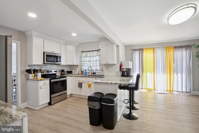 kitchen with white cabinetry, light stone counters, a breakfast bar area, and stainless steel appliances