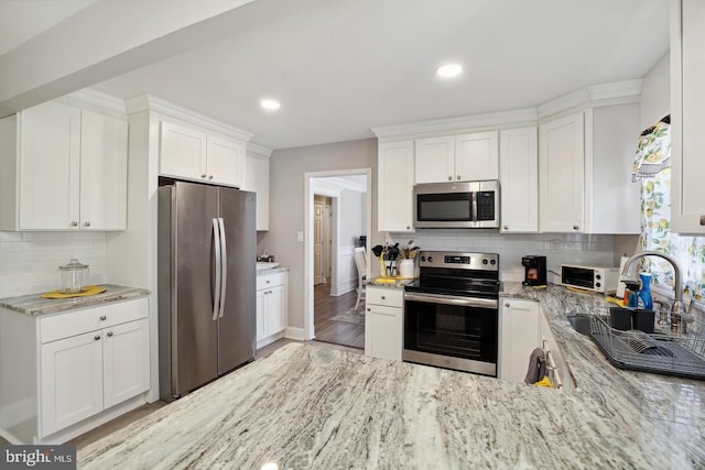 kitchen featuring stainless steel appliances, light stone countertops, white cabinets, and backsplash