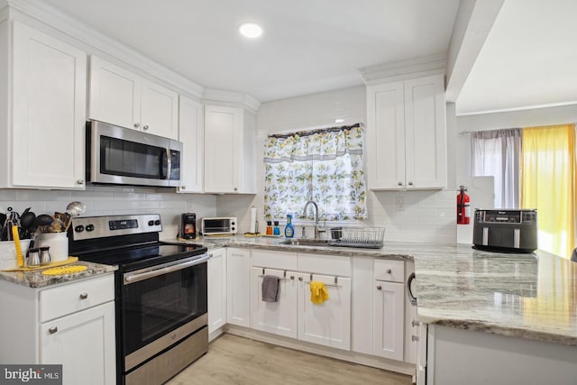 kitchen featuring sink, backsplash, stainless steel appliances, light stone counters, and white cabinets