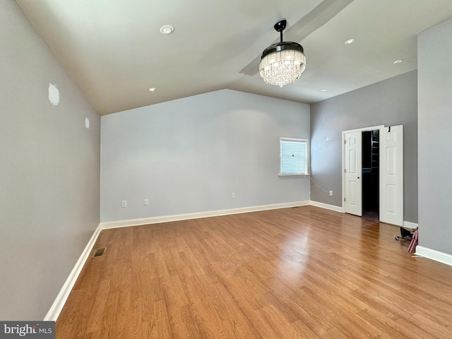 spare room featuring a notable chandelier, vaulted ceiling, and light wood-type flooring