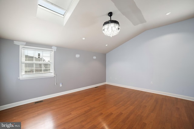 spare room featuring a notable chandelier, hardwood / wood-style flooring, and lofted ceiling with skylight