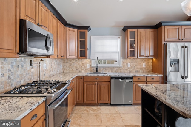 kitchen with light tile patterned flooring, sink, light stone counters, appliances with stainless steel finishes, and backsplash