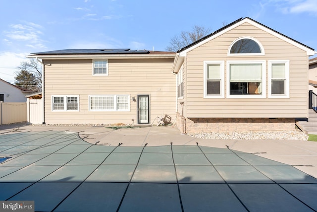 rear view of property featuring a covered pool, a patio area, and solar panels