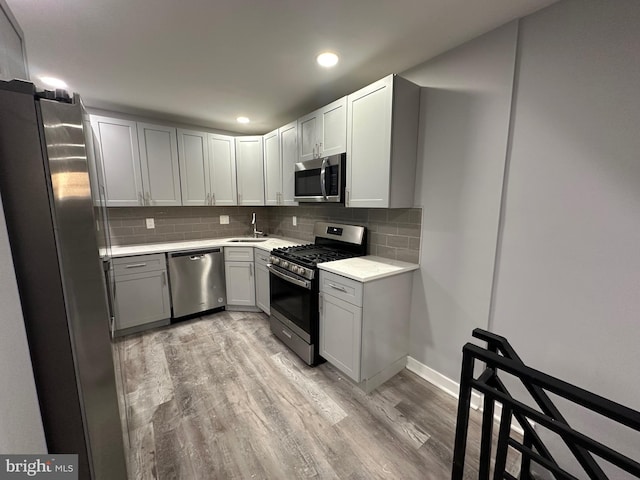 kitchen featuring gray cabinets, sink, backsplash, stainless steel appliances, and light hardwood / wood-style flooring