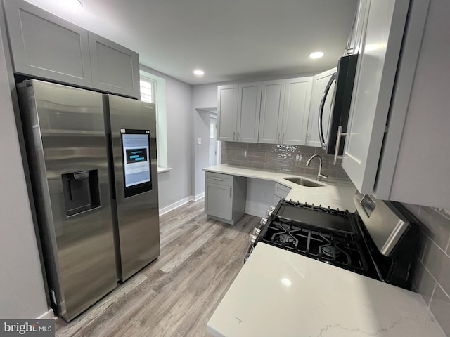 kitchen featuring appliances with stainless steel finishes, sink, gray cabinetry, backsplash, and light hardwood / wood-style flooring