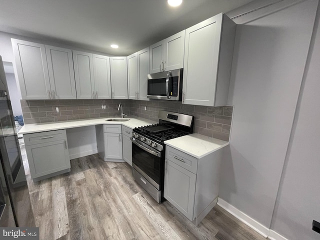 kitchen featuring appliances with stainless steel finishes, gray cabinetry, decorative backsplash, and light hardwood / wood-style flooring