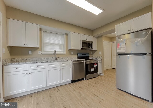 kitchen featuring appliances with stainless steel finishes, sink, white cabinets, light stone countertops, and light hardwood / wood-style flooring