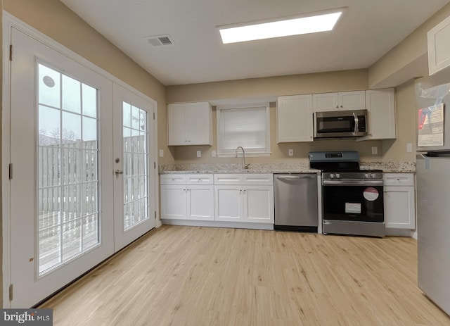 kitchen with stainless steel appliances, sink, white cabinets, and light hardwood / wood-style flooring